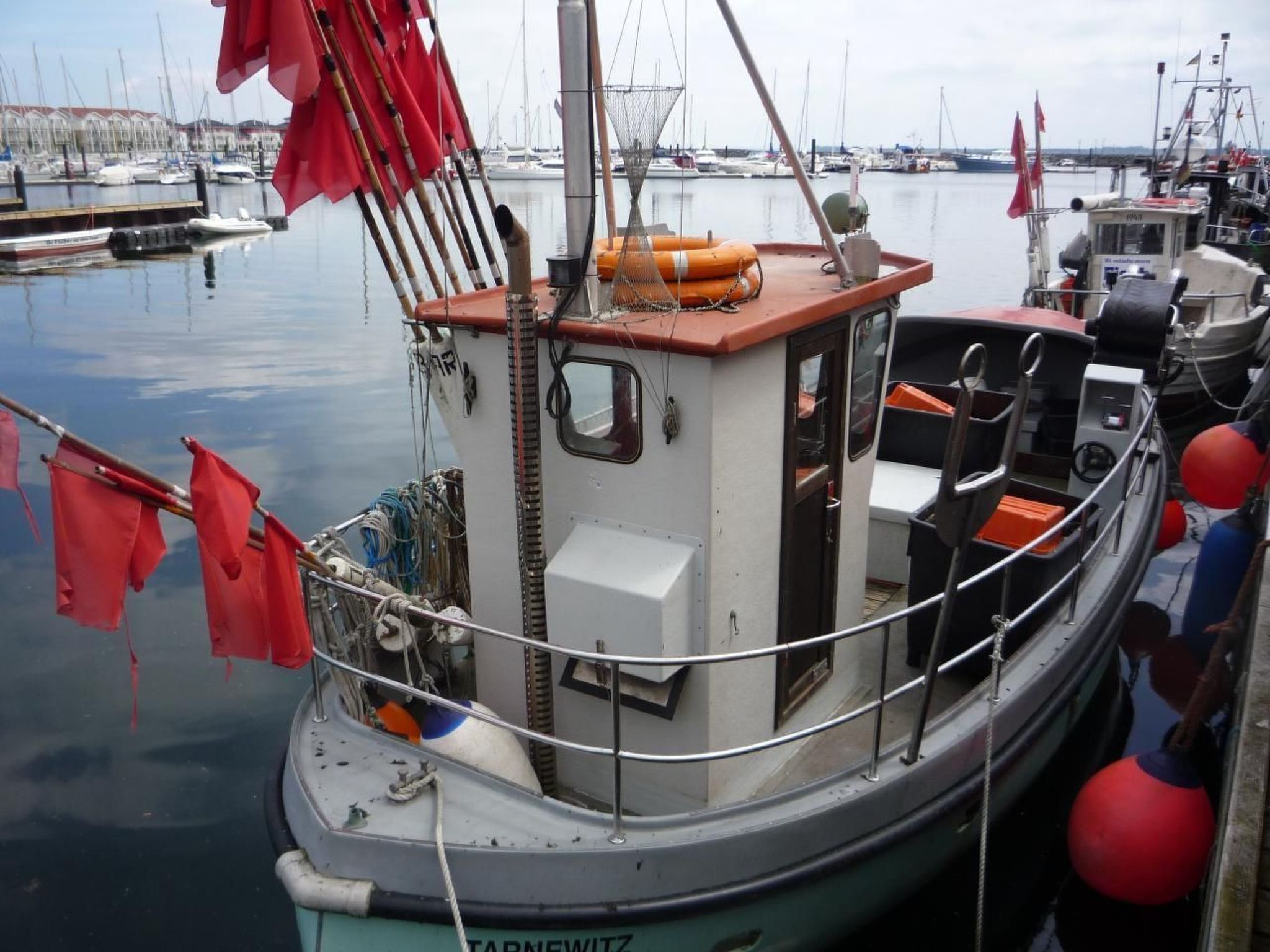 Een boot afgemeerd in een jachthaven, met een hut, zitgedeelte en diverse apparatuur.