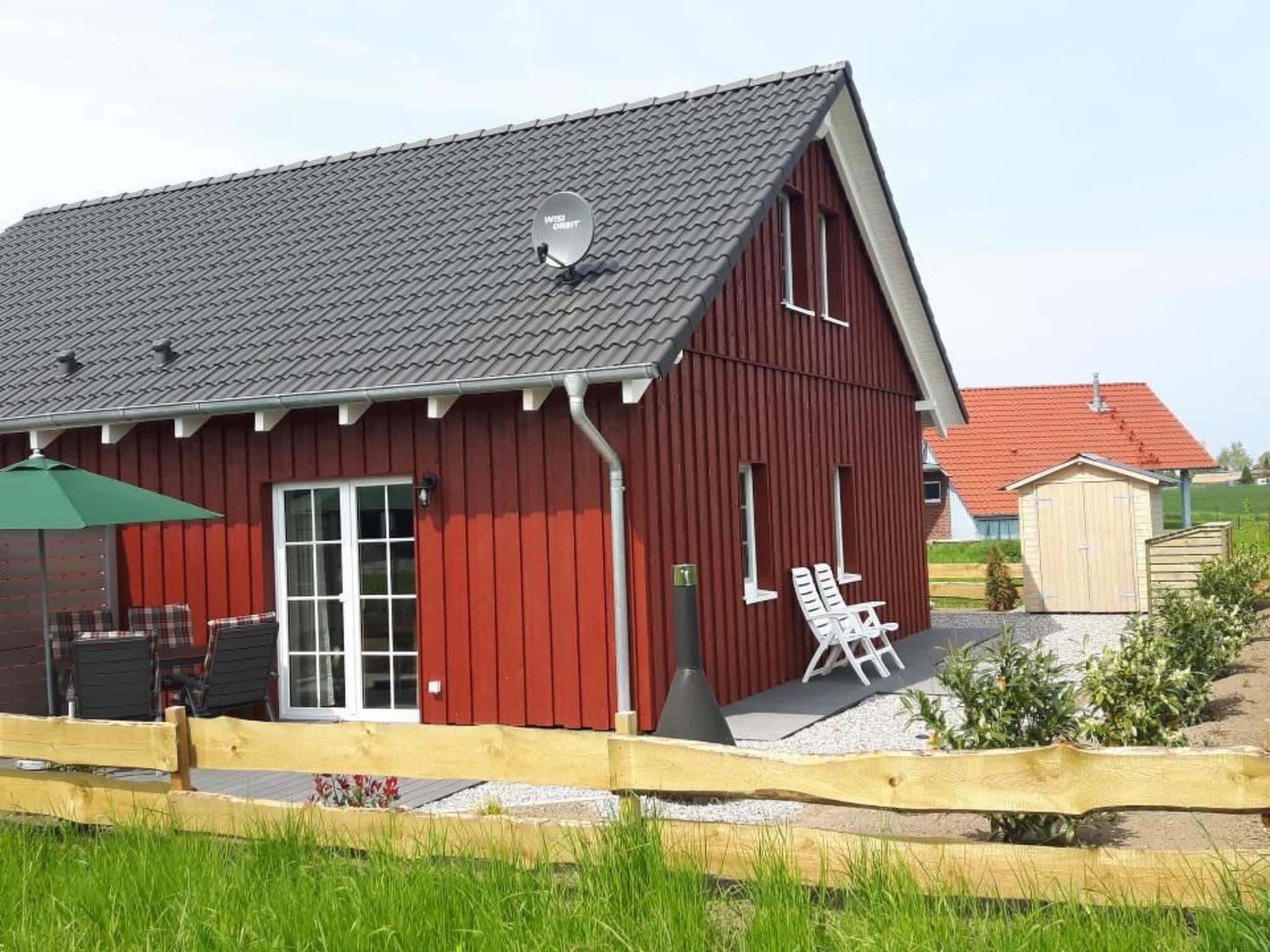 Een rode schuur met een schuin dak, een schotelantenne en een klein terras met twee stoelen.