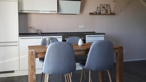 A modern kitchen with white cabinets, a wooden dining table, and two grey chairs. - Schwedenhaus Zierow mit Terrasse und Grill by Interhome (Alt Jassewitz)