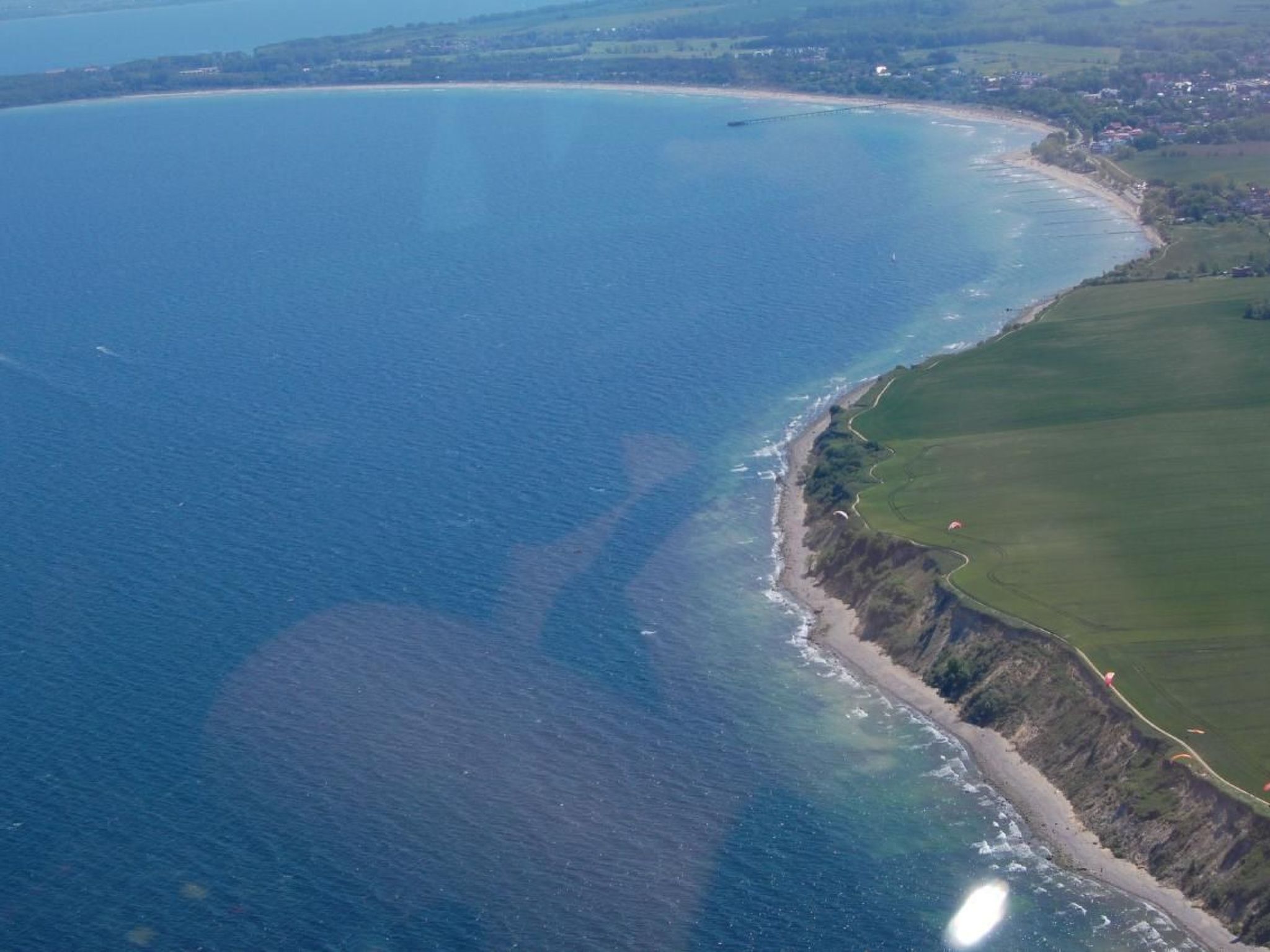 An aerial view of a coastal area with a beach, cliffs, and a golf course.