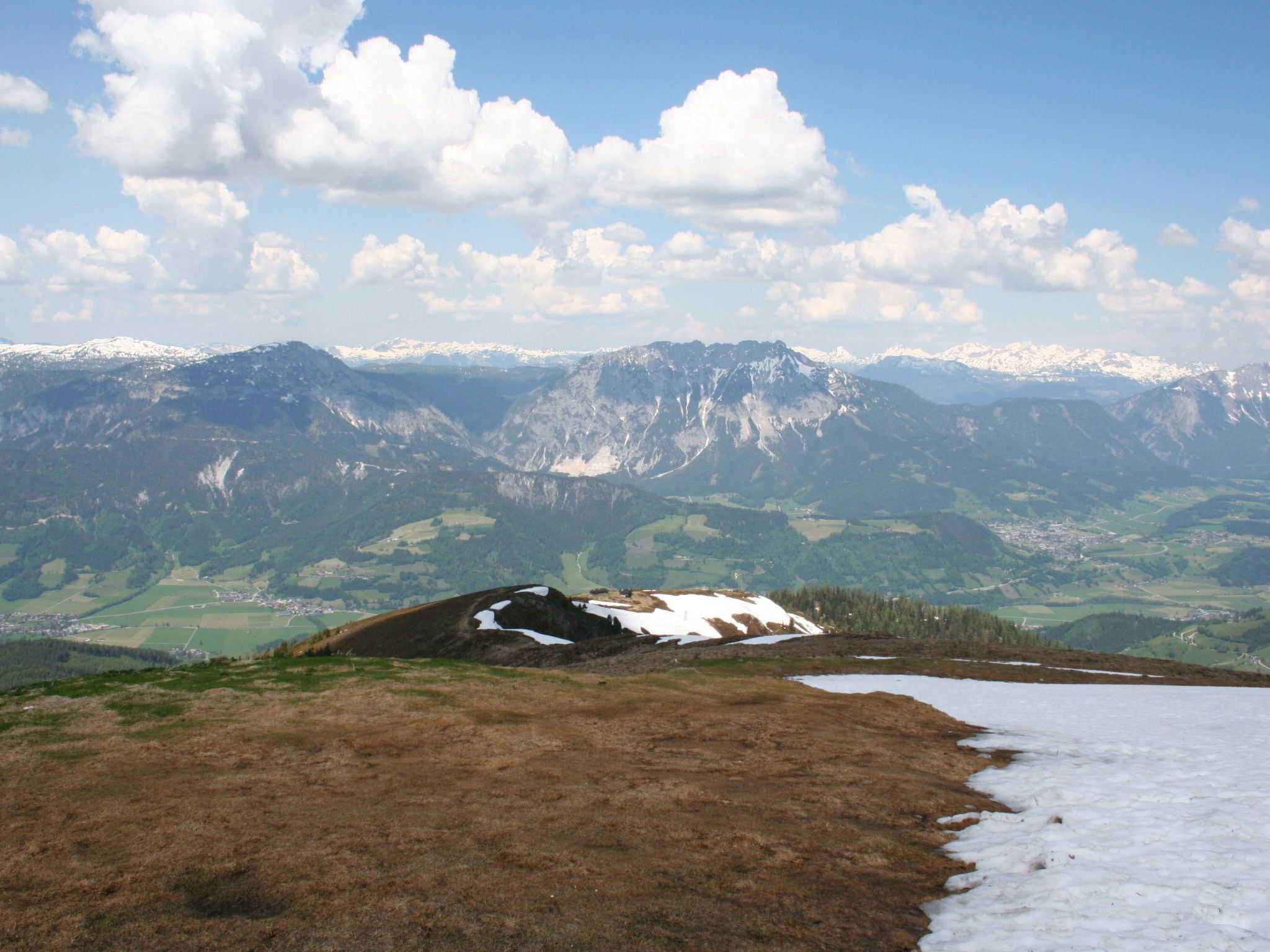 Eine gebirgige Landschaft mit einem Tal, Schneeflecken und blauem Himmel.
