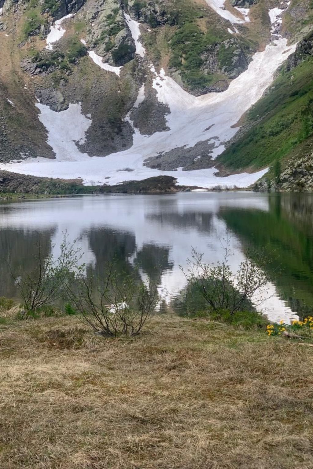 A calm lake surrounded by rocky mountains with patches of snow.