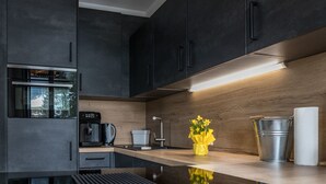 Een moderne keuken met donkere kastjes, een roestvrijstalen oven, een koffiezetapparaat en een houten aanrecht.