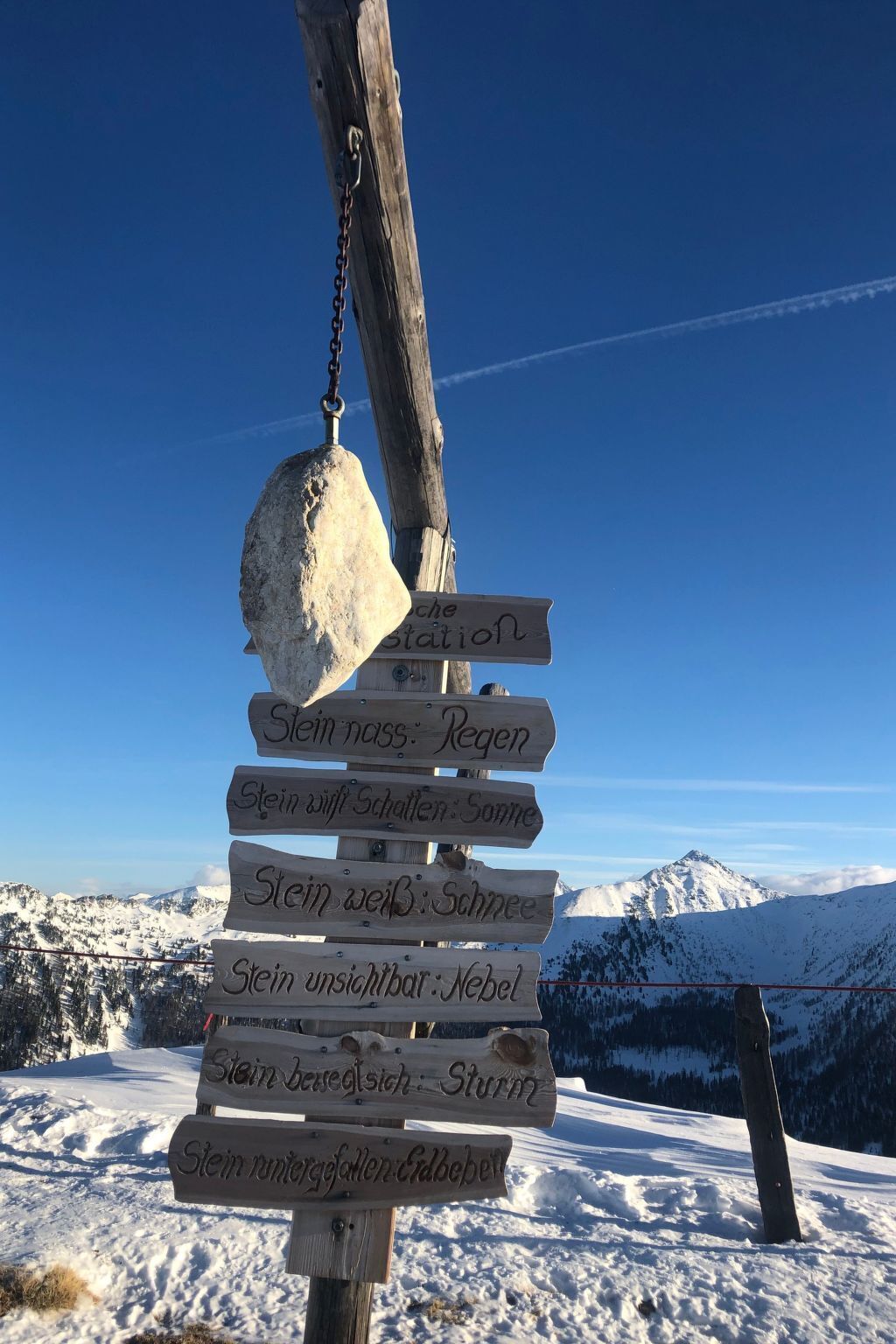 A wooden signpost with multiple directional signs in a snowy landscape with mountains in the background.