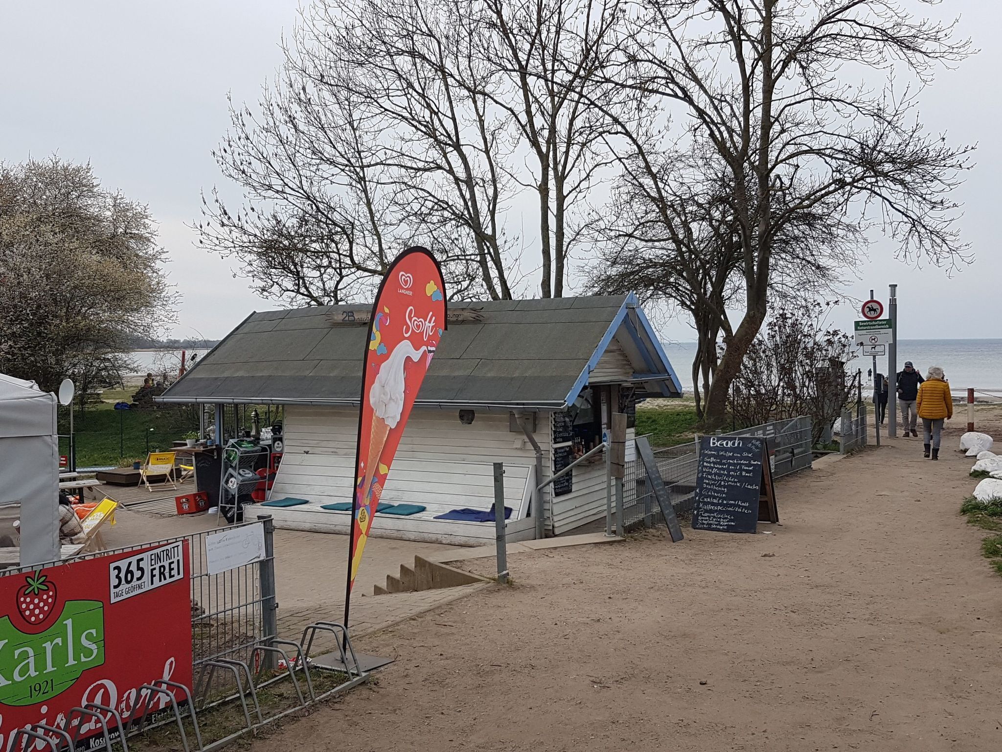 A beachside kiosk with a sign advertising ice cream, a small building with a sloped roof, and a sandy path leading to the beach.