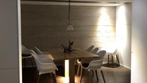 Un coin repas avec une table en bois et des chaises blanches, un luminaire suspendu et un mur en bois en arrière-plan.
