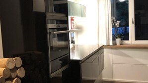 Une cuisine moderne dotée d’appareils électroménagers intégrés, d’un présentoir à bois et d’une fenêtre agrémentée de rideaux.