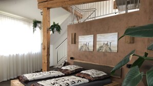 Un lit avec un cadre en bois et un matelas foncé, un escalier avec une rampe en métal, et deux tableaux accrochés au mur représentant une jetée.
