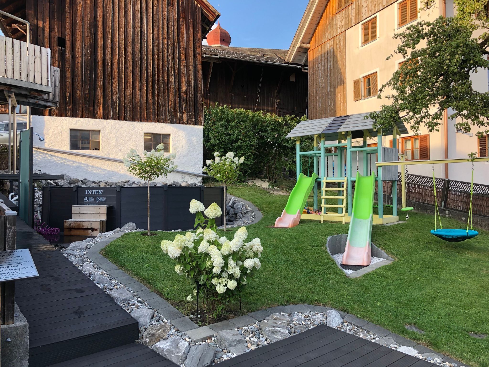 A residential area with a playground, a wooden barn, and a white building with a small window.
