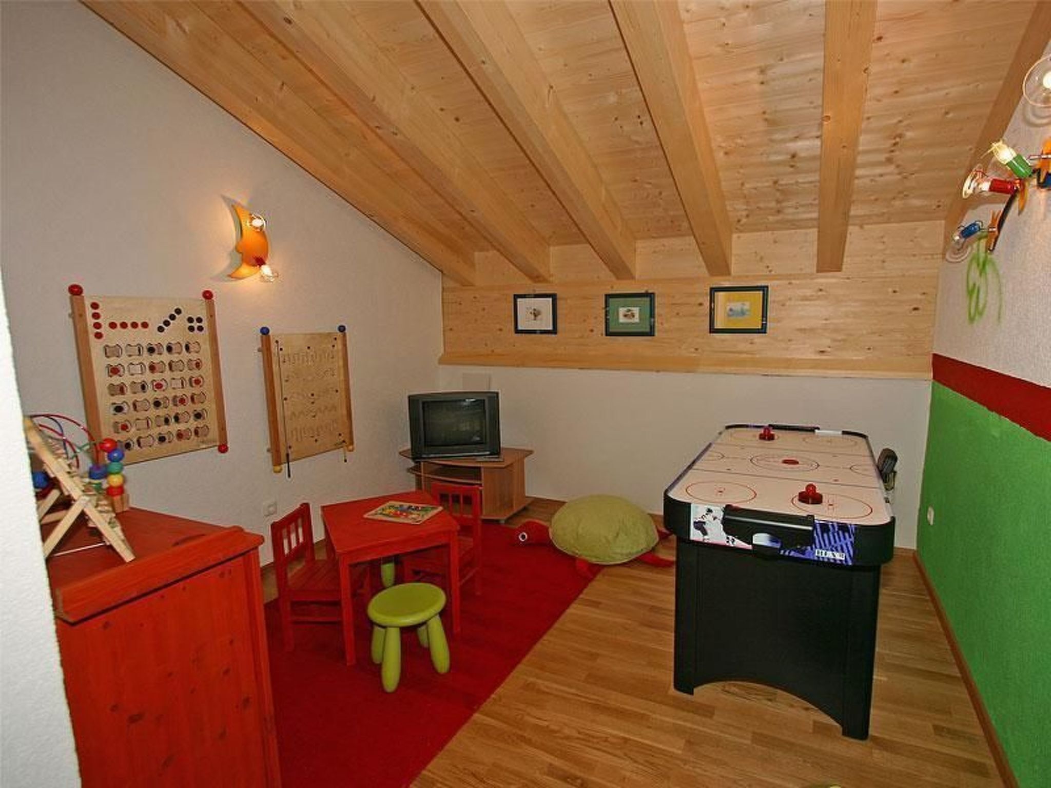 Ein gemütliches Zimmer mit Holzbalkendecke, einem Kicker, einem Fernseher und einem roten Sessel.