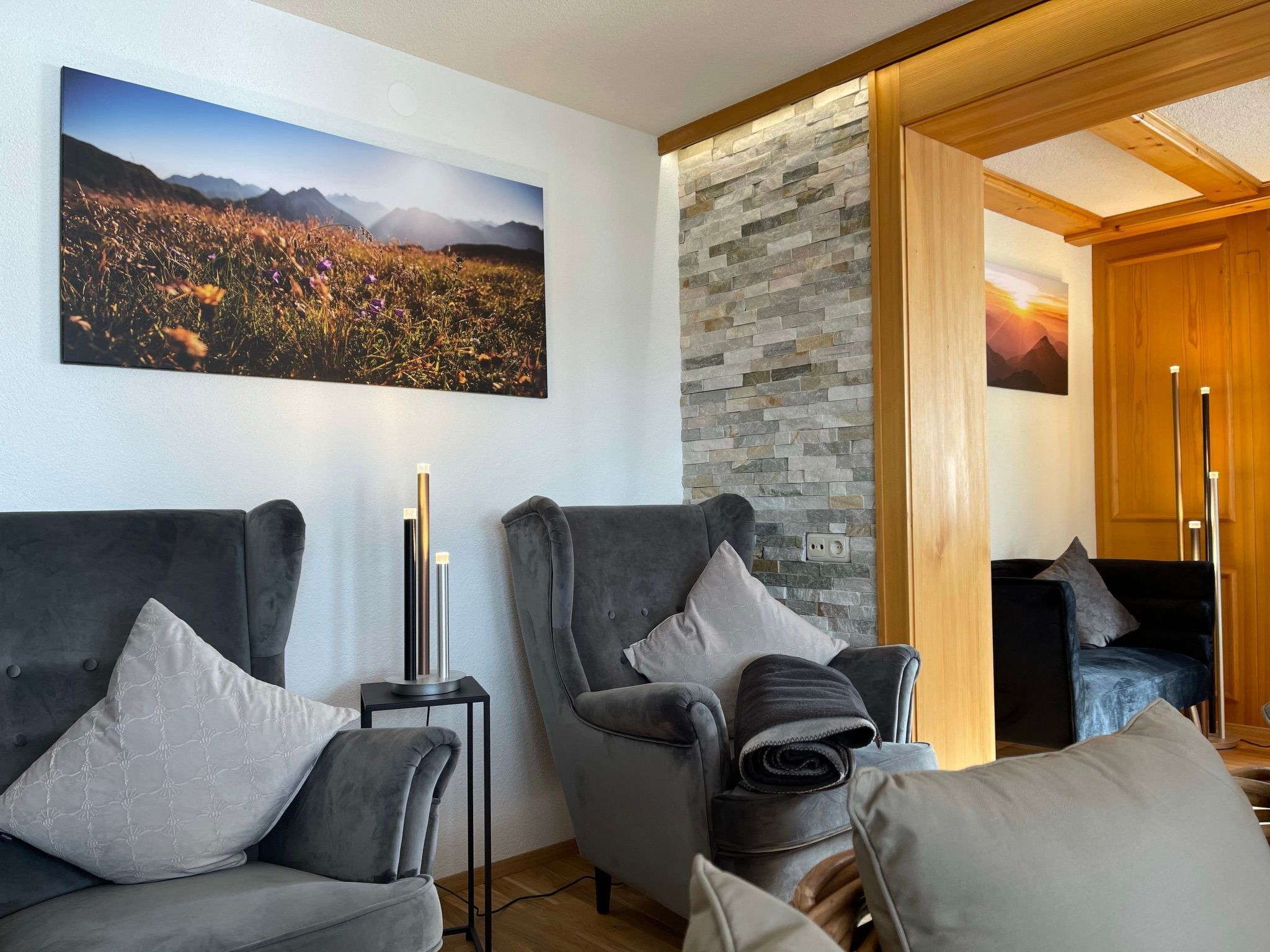 Een moderne woonkamer met twee grijze banken, een accentmuur van natuursteen en een groot landschapsschilderij.