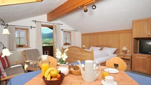 Ein gemütliches Hotelzimmer mit einem hölzernen Bett, einem mit Frühstück gedeckten Esstisch, einem Fernseher und Blick ins Freie.