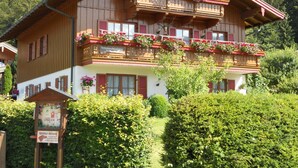 Eine traditionelle Holzhütte mit Balkonen, die mit Blumen geschmückt sind, umgeben von üppiger Vegetation.