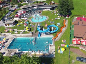 An aerial view of a water park with a large pool, a water slide, and sun loungers. - in Dorfgastein by Interhome (Dorfgastein)