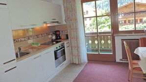 Une cuisine avec des meubles blancs, une cuisinière et une machine à café. Il y a une fenêtre qui donne sur des immeubles et des arbres.