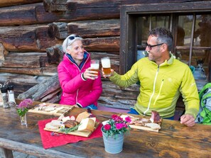 Une table en bois avec de la nourriture et des boissons, un chalet en bois en arrière-plan et une fenêtre.