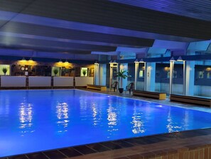 Una piscina interior con agua cristalina, rodeada de paredes con ventanas y puertas, y un techo con diseño de cuadrícula.