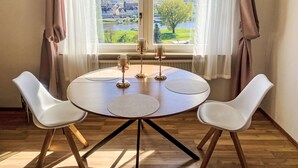 Een eettafel met twee stoelen, uitzicht op een rivier en gebouwen, en een raam met gordijnen.