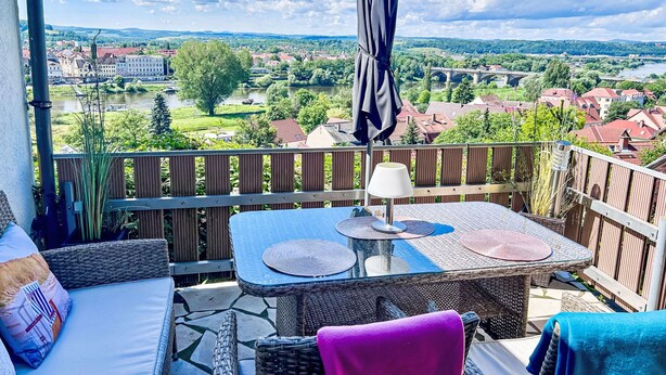 Een balkon met rieten meubels, een tafel en een parasol.