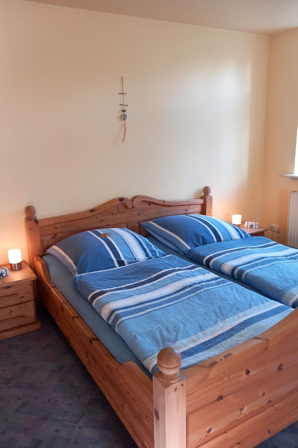 Ein hölzernes Bett mit blau gestreifter Bettwäsche in einem Raum mit schlichter Wand und einem kleinen Nachttisch mit Lampe.
