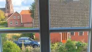 Ein Fenster mit Blick auf eine Kirche, ein rotes Haus und ein blaues Auto.