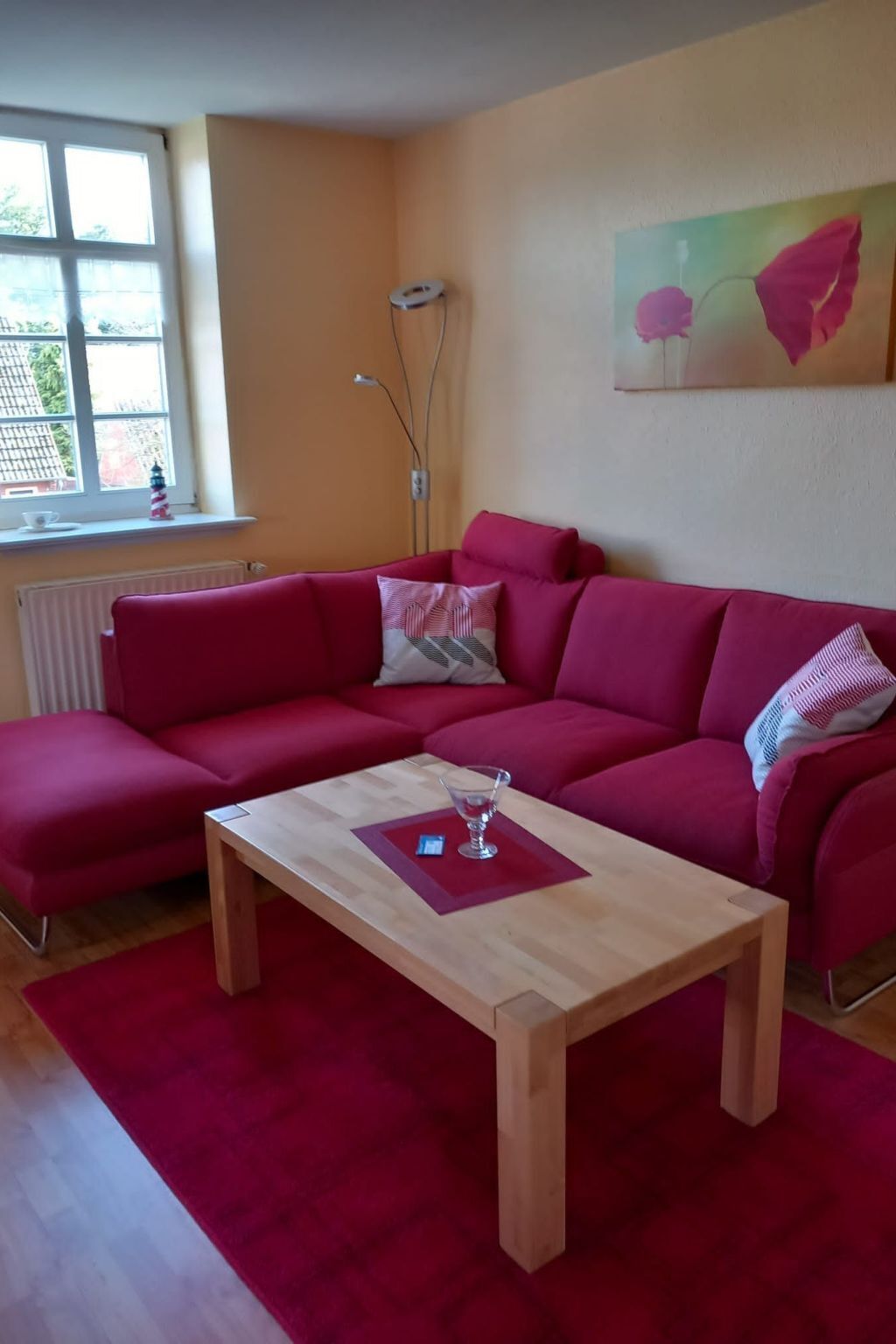 Ein Wohnzimmer mit einem roten Ecksofa, einem Holztisch und einem Fenster mit Blick auf Bäume.