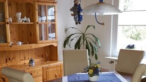 Un comedor con una mesa y sillas de madera, una planta en maceta y un armario de madera con puertas de cristal.