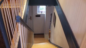 Una escalera de madera con barandilla que lleva a una puerta con un pequeño ventanal.