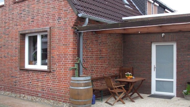 Una casa de ladrillo con techo de tejas, una ventana, una puerta y un pequeño patio con mesa y sillas.