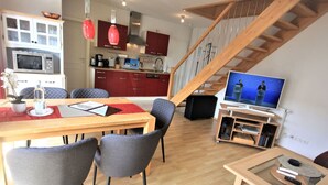A modern kitchen with a microwave, stove, and red cabinets. There is a dining area with a wooden table and grey chairs. A TV is mounted on the wall, and a staircase leads to an upper level. - Wohnung in Koserow mit Garten und Grill und Neben dem Strand by Interhome (Koserow)