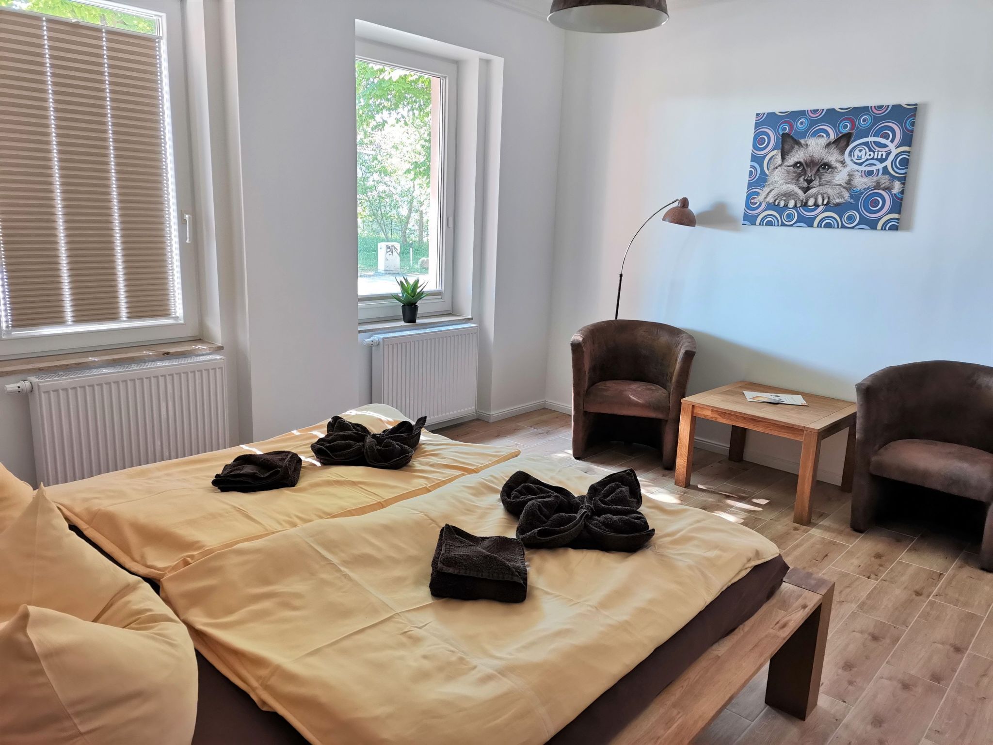 Ein Zimmer mit einem Bett, zwei Sesseln, einem kleinen Tisch und einem Fenster mit Jalousien.