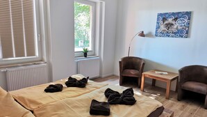 Ein Zimmer mit einem Bett, zwei Sesseln, einem kleinen Tisch und einem Fenster mit Jalousien.