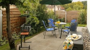 A patio with a table and chairs, an umbrella, and a small cart. - Vacation home  by Interhome (Bansin)