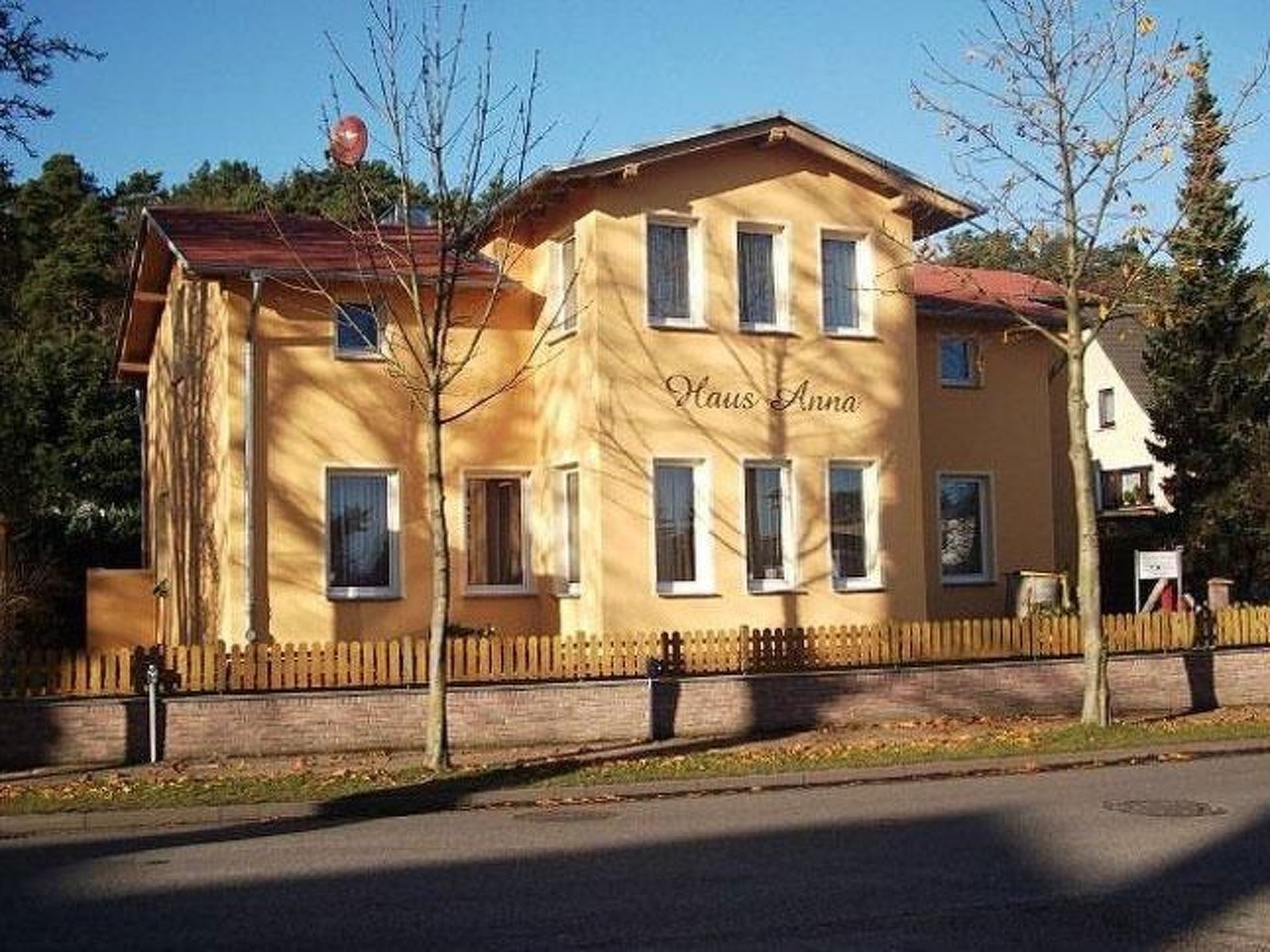 En tvåvåningsbyggnad med en gul fasad, flera fönster och ett trästaket framför.