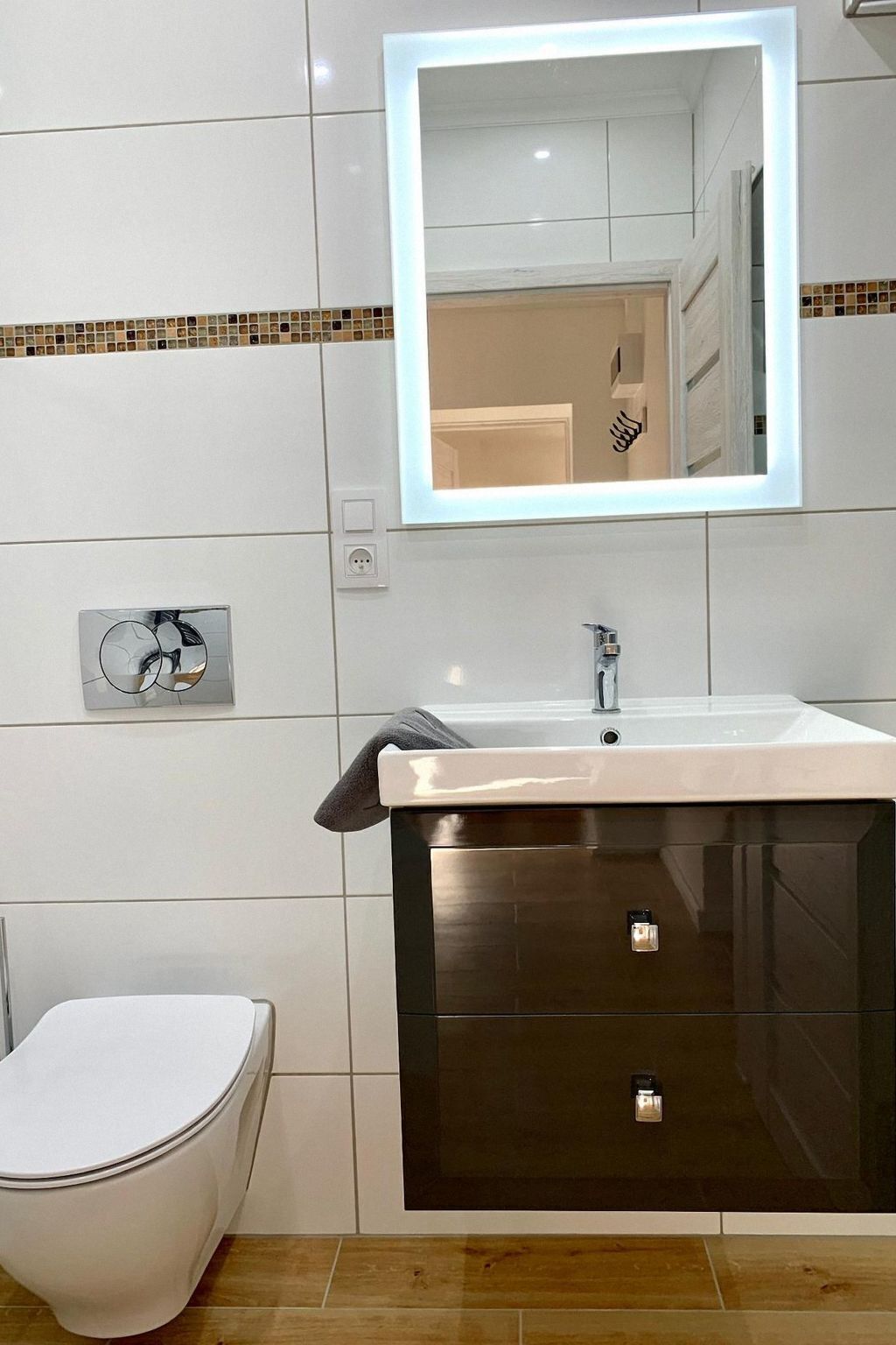 Un baño moderno con inodoro blanco, un lavabo con mueble oscuro y un espejo sobre el lavabo.