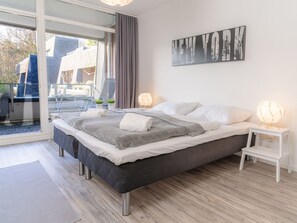 Ett modernt sovrum med en stor säng, ett konstverk som föreställer en stadsbild och en utsikt genom en glasdörr.