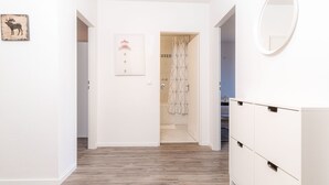 Käytävän lattia on parkettia, siellä on valkoinen vaatekaappi, kehystetty kuva hirvestä ja ovi, joka johtaa kylpyhuoneeseen, jossa on geometrisesti kuvioitu suihkuverho.