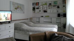 Un dormitorio con cama, televisor, estantería y cómoda.
