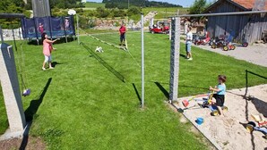 Een achtertuin met een volleybalnet, een trampoline en een zandbak.