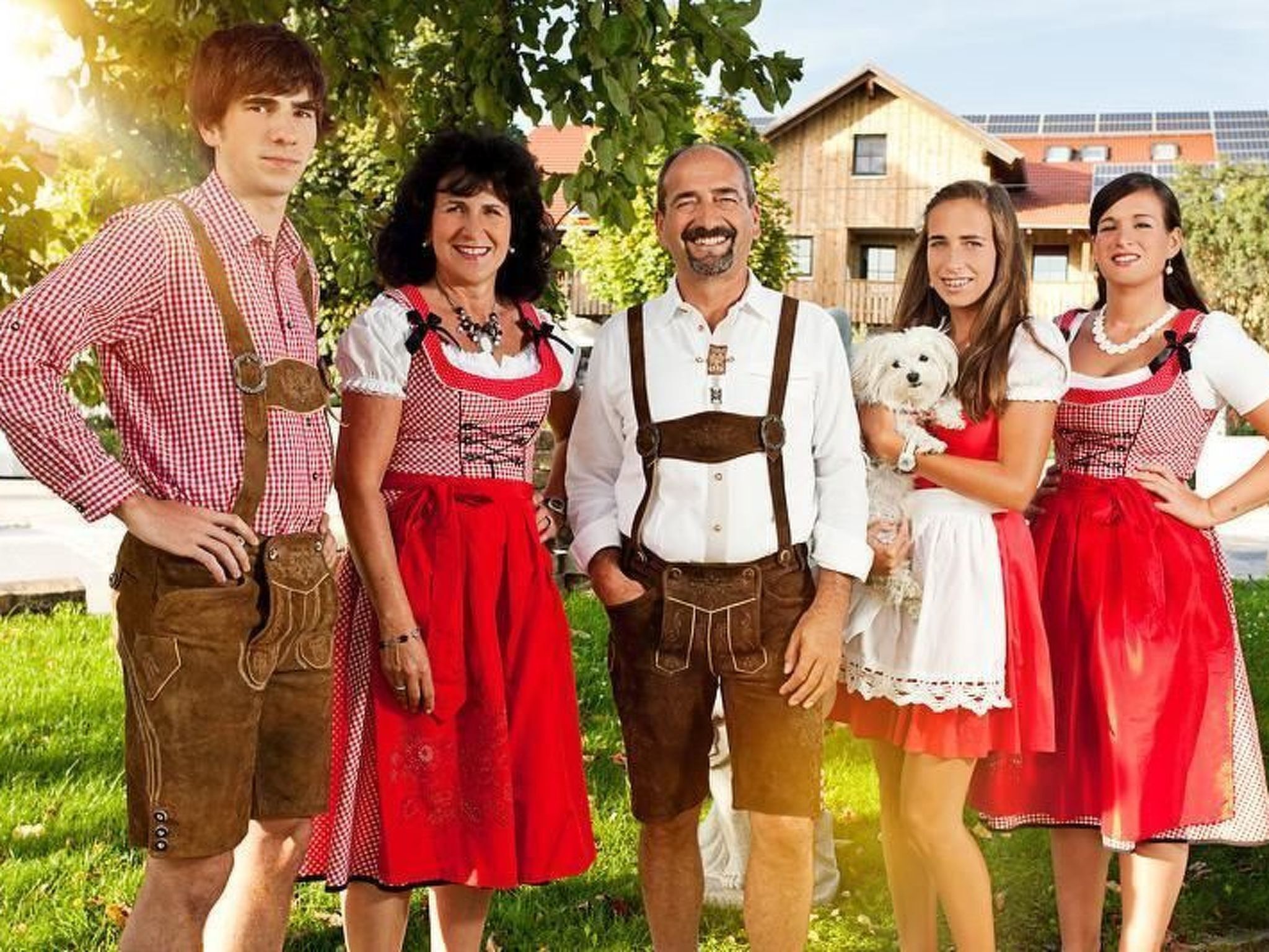 Un groupe de personnes, vêtues de costumes traditionnels, se tient à l’extérieur, avec une maison en arrière-plan.