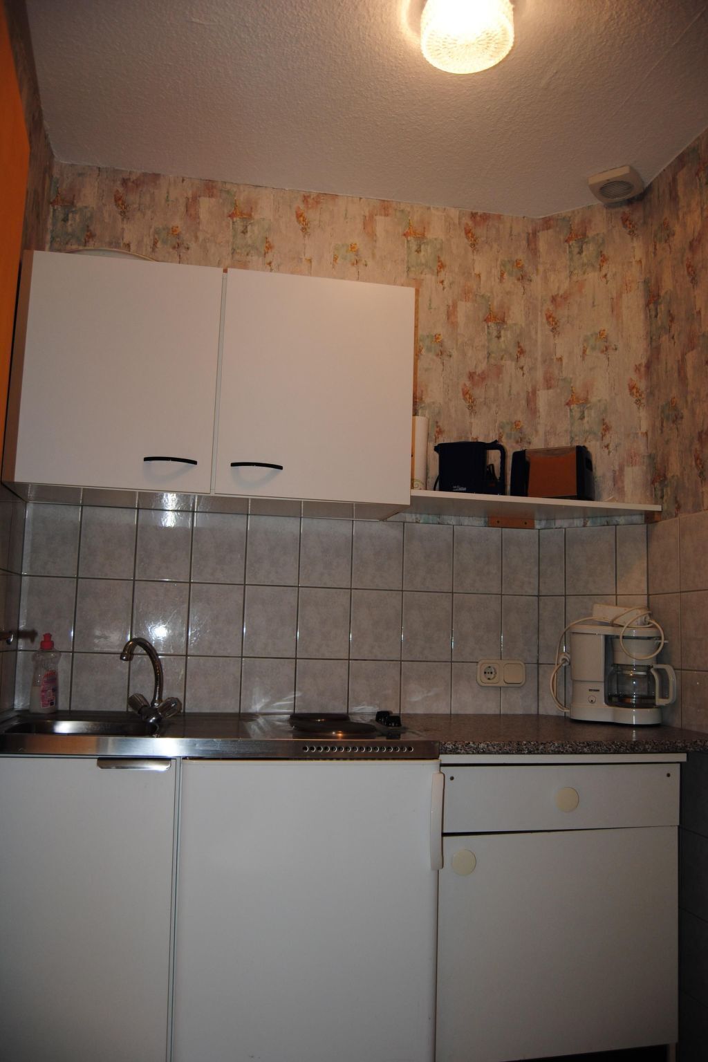 Cozinha com armários brancos, painel de azulejos, cafeteira e chaleira.