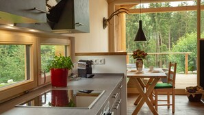 Une cuisine moderne dotée d’une grande fenêtre, un coin repas avec une table et des chaises, et une vue sur la forêt environnante.