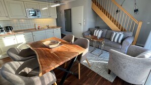 A modern kitchen with white cabinets, a wooden dining table, and a grey sofa. - Wohnung mit Sonnenbalkon und Strandnähe by Interhome (Wenningstedt-Braderup)