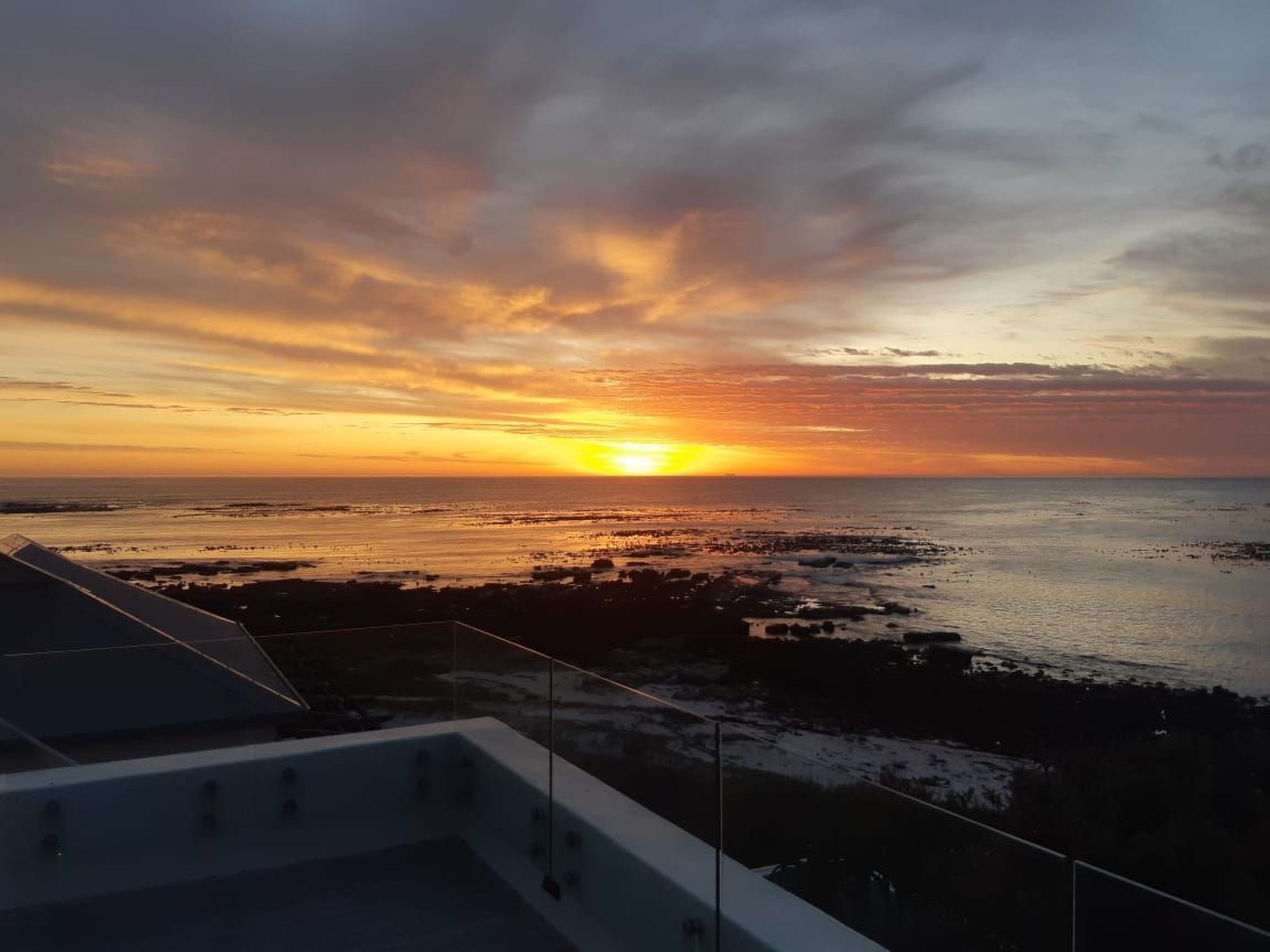 Vista do pôr do sol a partir de uma varanda com vista para uma praia, sob um céu limpo.