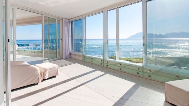 Ein modernes Schlafzimmer mit einem großen Glasfenster, das auf einen Balkon mit Blick aufs Meer führt.