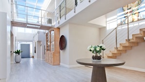 Ein großzügiges, modernes Interieur mit hoher Decke, einer Treppe und einem runden Tisch mit Blumen.