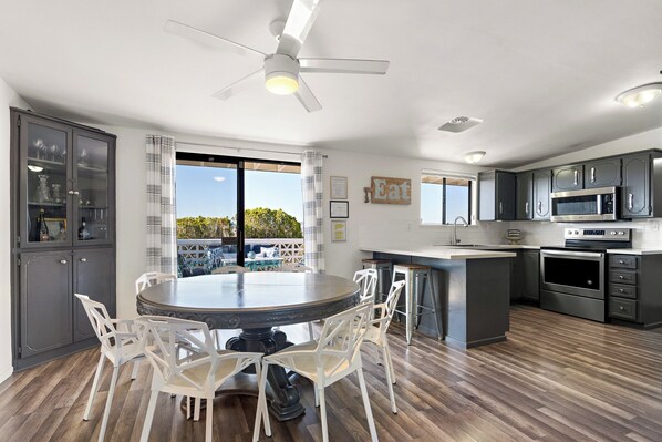 A modern kitchen with a dining area, featuring a round table, white chairs, and a view of the outdoors. - Pool, pickleball, views, stars, sunsets, perfect (Twentynine Palms)