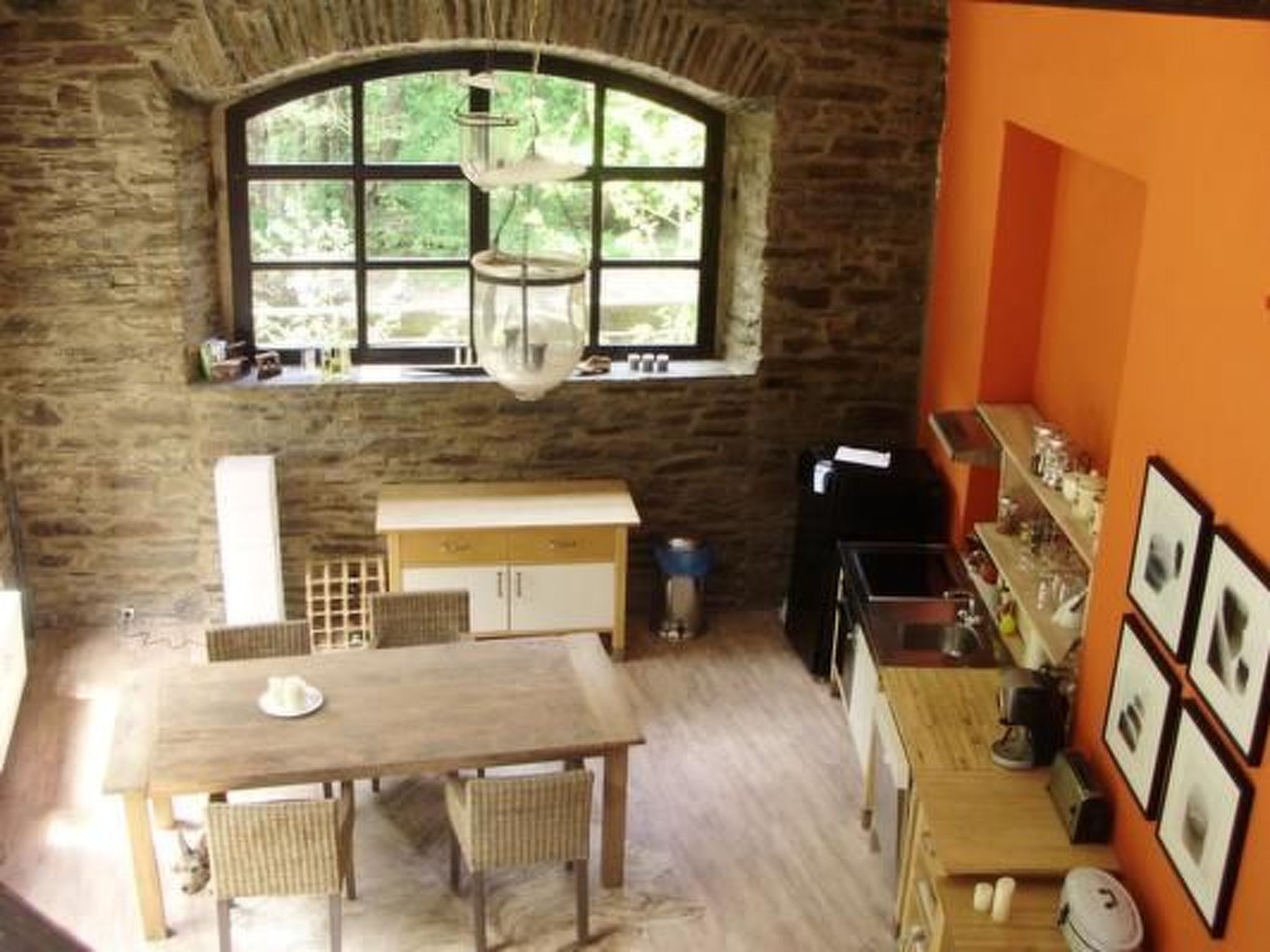Eine rustikale Küche mit Steinwand, großem Fenster, Holztisch und Regal mit gerahmten Bildern.