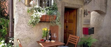 Une terrasse extérieure avec une table en bois et deux chaises, une plante suspendue et une porte portant l’inscription « CASA AL VENTO ».
