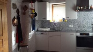 Une cuisine avec des meubles blancs, un four encastré et une fenêtre avec des stores.